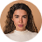 Young woman with curly hair wearing a green outfit, posing against a red background.